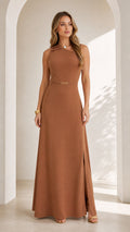 Front full view of woman wearing caramel brown sleeveless asymmetrical maxi dress with chain waist detail