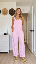 Model wearing pink wide-leg bib overalls with adjustable straps and rolled hems