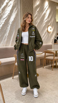 Model wearing olive green racing graphic zip-up jacket and wide-leg track pants set